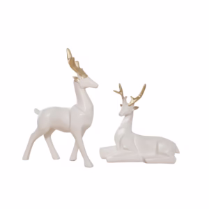 Two white ceramic deer figurines with golden antlers placed on a reflective black surface against a white and black background. One deer is standing while the other is lying down.